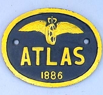 Oval skylt av järn med gul text och vinghjulssymbol på svart botten. Text: "Atlas 1886".