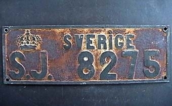 Två stycken rektangulära skyltar av gjutjärn med svart text på vit botten: "SVERIGE S.J. 8275". Mycket rostig.
Från godsvagn.