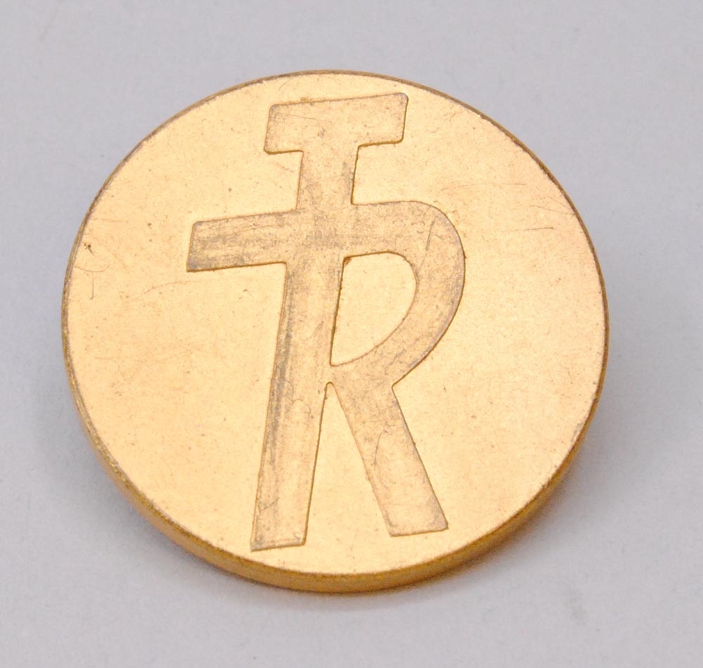 Knapp av guldfärgad metall med TR:s logotyp med bokstäverna "TR" sammanlänkade i relief i form av logotypen "TR-pojken". På baksidan av knappen står det "* C.C. SPORRONG & CO. * STOCKHOLM". 

Se även Jvm15380.