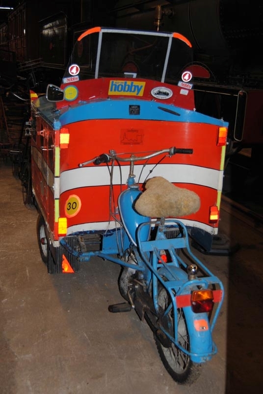 Trehjulig moped som är omgjord för att likna ett Rc-lok. Skåpet är målat orange med svarta fält som föreställer fönster, turkos tak, ett vitt fält med svarta kantlinjer mitt på med texten "TÅGET FRAMFÖR ALLT" i turkos och en vit och en blågrå kant nedtill där det står "A" och "Rc 1000" med vita bokstäver. I takets främre hörn sitter rödgul randiga skärmar. Mitt fram sitter en grå och röd tuta. På taket sitter en vindruta av plast med flera klisterdekaler på. Dekalerna på framsidan av vindrutan är symmetriskt uppsatta på var sida och föreställer TV4s symbol "4", en blixt som är symbol för elektricitet och dekaler med texten "allt om hobby". På insidan sitter också reklam dekaler från TV4, Allt om hobby samt en dekal med ett ånglok från TGOJ och en dekal från Sundbyberg. På skåpet, till vänster framför mopeden, sitter en dekal som föreställer en hastighetsskylt för 30 km/tim. Taket går att öppna som en lucka och har öglor för hänglås på vänster sida. På vänster sida sitter en backspegel. Mopeden är turkos. Sadeln har ett skydd av fårskinn. Framtill sitter lyktor och buffertar, målade svarta fönster med konstgjorda vindrutetorkare, en SJ klisterdekal i mitten och "1000" målat på sidorna. Plog finns i skåpet.