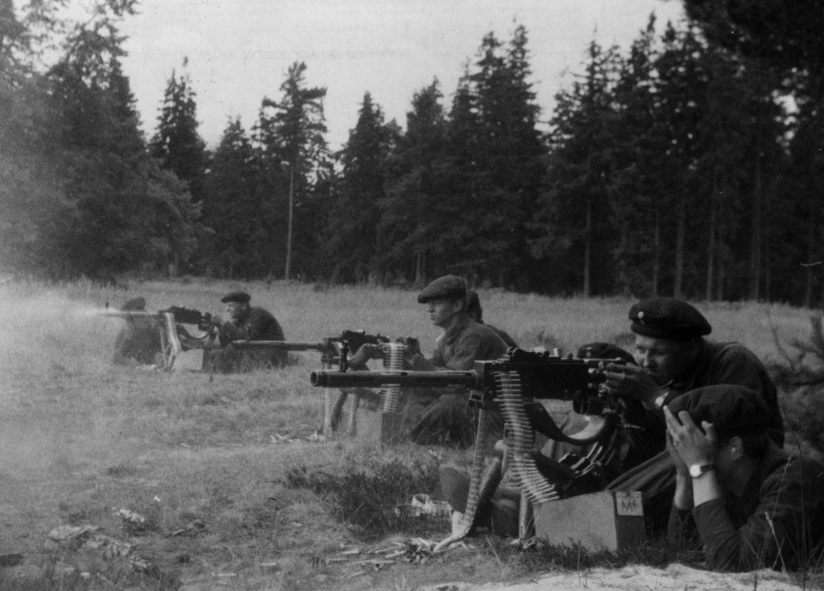 Skjutning med Ksp m/39 strv i marklavett på Utö skjutfält. Skytten närmast är 105 Andersson, nästa är 810 Ekman.
Ksp m/39 var konstruerad för, och fungerade bäst med, 8 mm ammunition. Nu var den am på utgående och skulle ersättas av 6,5 mm am (samma som till gevär m/96). Så vår am var nu "gratis" och vi fick skjuta hur mycket som helst. 
Efter att Ak 4 (automatkarbin) införts i Armén byttes piporna senare till 7,62 mm (308 Win).
Efter 250 skott var pipan så varm att den måste bytas. Kommer ihåg att reservpiporna brände gräset ordentligt när vi lade dem på marken.