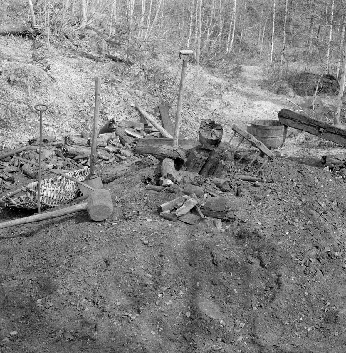 Kolbotn hos smeden Jørgen eller Jørn Romundstad (1890-1972) på Vegårshei i Aust-Agder.  Bildet skal være tatt våren 1968 mot den sirkelformete kolbotnen, der Romundstad hadde rakt kolbitene ut mot sidene.  På opptakstidspunktet lå det bare noen få kolbiter igjen i sentrum av kolbotnen.  Ved siden av lå redskapene som ble brukt under kolbrenninga.  Vi ser et flettet kolfat, et spett, en spade, et spett, ei treklubbe og to river med ulik tinnelengde.  I bakgrunnen ser vi også ei avskjæring av tre som inneholdt vann, for slokking dersom det skulle blusse opp varme i kolbitene.  Mot denne avskjæringa lå det ei «stubbehylle», et T-formet treelement som skulle hindre at dekket på de bratte sidekantene av mila raste ned og skapte åpninger der det kunne sive inn oksygenrik luft som kunne sette kolveden i brann. Ei kort orientering om kolbrenning i slike miler finnes under fanen «Opplysninger». Trekolbrenning. Kullmile. Mile. Kolmile.