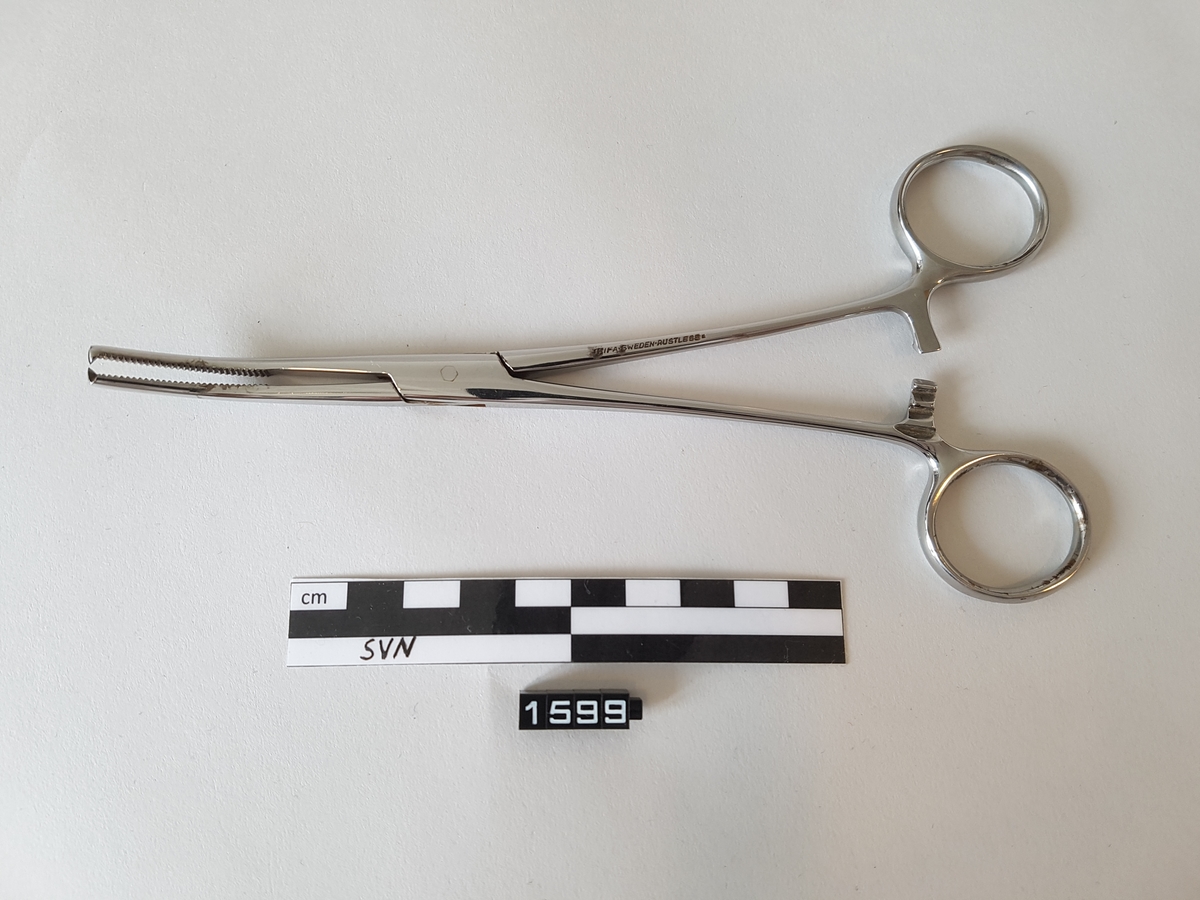 Gjenstanden er en kirurgisk bøyd klemme. 
Klemmen er utformet som en saks, men i stede for skjærekniver er det to flater som møtes og klemmes sammen.
Flatene som møtes har serrateringer, riller. ytterst på klemmen har flatene tenner som går i hverandre.
To tenner på en side og en tann på den andre siden.
Gjenstanden har fingerhull for manipulering av objektet.
like over fingerhullene er det en låsemekanisme med en hake på den ene delen og flere motstående haker på den andre delen
Instrumentet kan låses ved hjelp av disse og hvor mye press det legges på tangspissen bestemmes av hvilken av mothakene 
det låses mot.