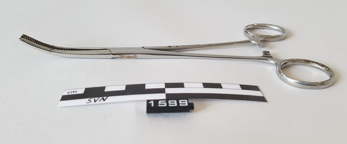 Gjenstanden er en kirurgisk bøyd klemme. 
Klemmen er utformet som en saks, men i stede for skjærekniver er det to flater som møtes og klemmes sammen.
Flatene som møtes har serrateringer, riller. ytterst på klemmen har flatene tenner som går i hverandre.
To tenner på en side og en tann på den andre siden.
Gjenstanden har fingerhull for manipulering av objektet.
like over fingerhullene er det en låsemekanisme med en hake på den ene delen og flere motstående haker på den andre delen
Instrumentet kan låses ved hjelp av disse og hvor mye press det legges på tangspissen bestemmes av hvilken av mothakene 
det låses mot.