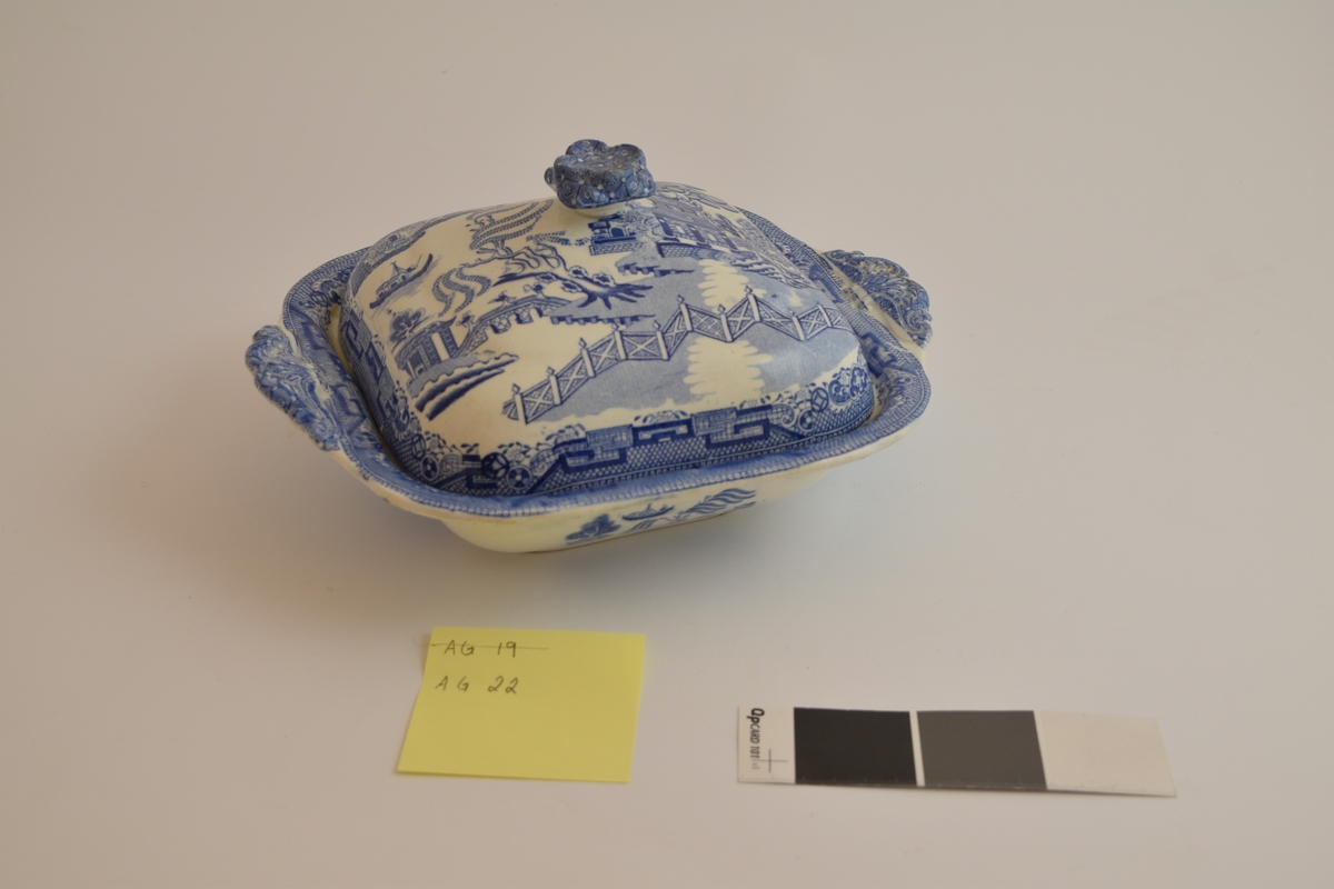 Fayanese lokkefat, leirgods med tinnglasur. Dekorert med en scene som framstiller flere hus, en elv, ett gjerde og dyr og planter. Stilen på dekorasjonen er asiatisk insprirert.