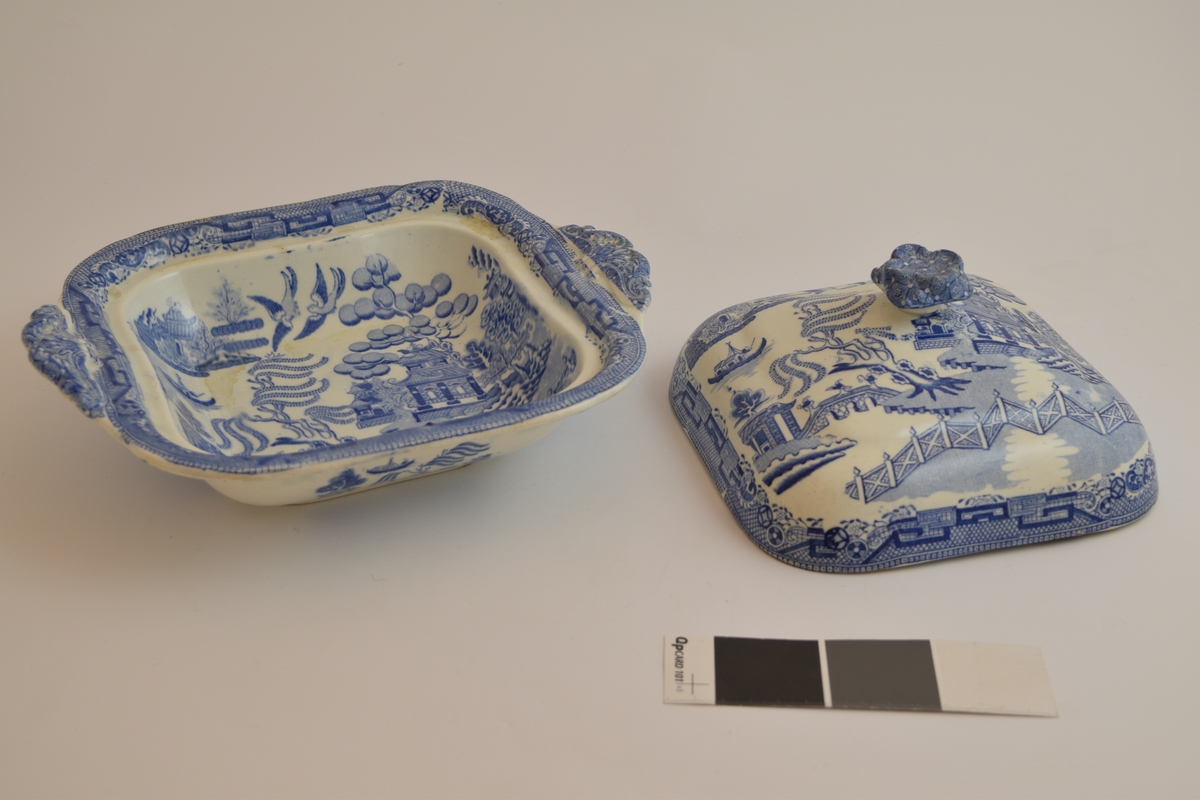 Fayanese lokkefat, leirgods med tinnglasur. Dekorert med en scene som framstiller flere hus, en elv, ett gjerde og dyr og planter. Stilen på dekorasjonen er asiatisk insprirert.