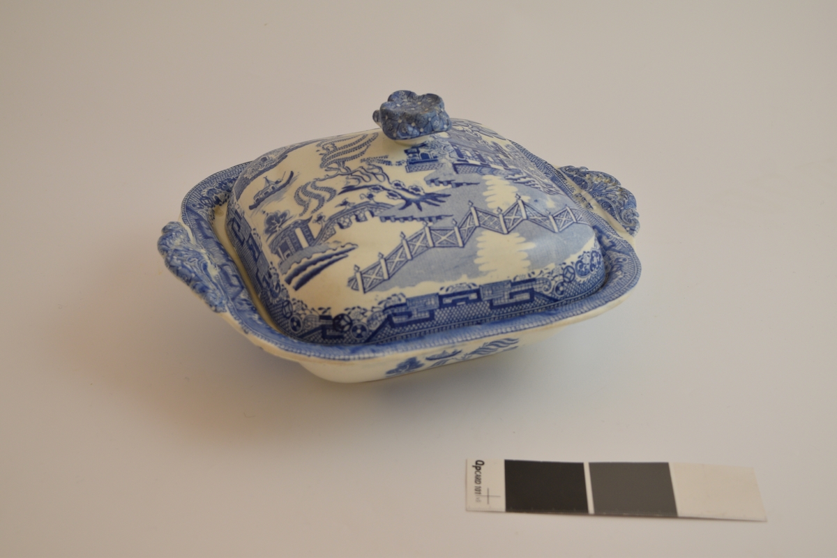 Fayanese lokkefat, leirgods med tinnglasur. Dekorert med en scene som framstiller flere hus, en elv, ett gjerde og dyr og planter. Stilen på dekorasjonen er asiatisk insprirert.