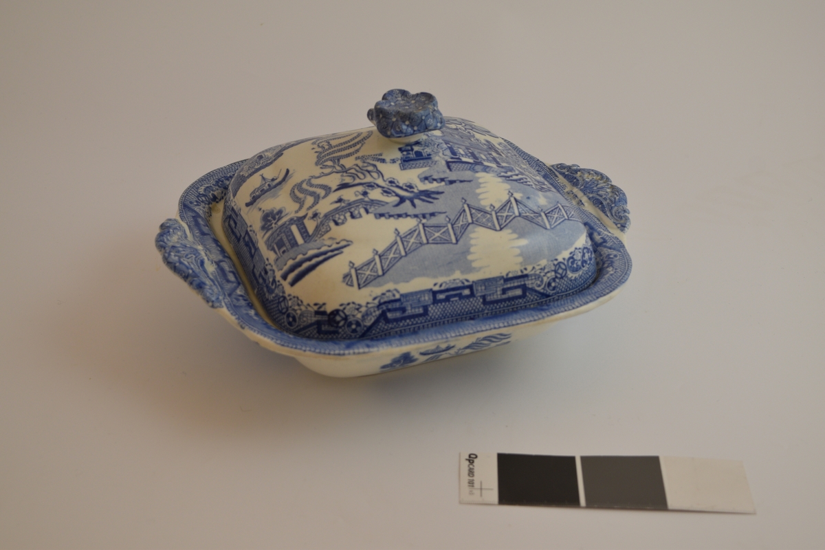 Fayanese lokkefat, leirgods med tinnglasur. Dekorert med en scene som framstiller flere hus, en elv, ett gjerde og dyr og planter. Stilen på dekorasjonen er asiatisk insprirert.