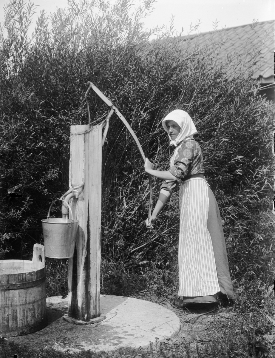 Kvinna vid vattenpump på Alinders gård, Sävasta, Altuna socken, Uppland i början av 1900-talet