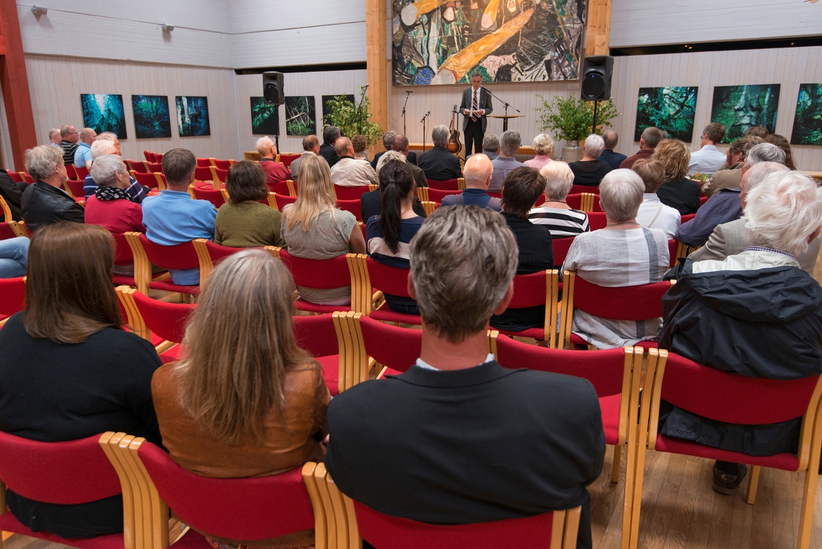 Fra åpningen av tredje og foreløpig siste byggetrinn av utstillingsprosjektet «Tråkk i mangfoldig natur» på Norsk Skogmuseum onsdag 4. juni 2014.  Utstillingen er bygd i tre faser.  Første byggetrinn – med presentasjoner av det norske naturmangfoldet, hovedlinjer i menneskets plass i denne naturen fra istida og fram til i dag, samt innføringer i naturforvaltning – ble åpnet i 2010.  Året etter ferdigstilte man en utstilling om mat basert på råvarer fra norsk natur.  Det siste byggetrinnet, som handler om jakt-, fangst-, fiske, og sankingstradisjoner, ble åpnet for publikum ved påsketider 2014, men den offisielle markeringa av begivenheten skjedde altså i begynnelsen av juni dette året.  Prosjektet (alle tre byggetrinn til sammen) hadde et budsjett på 12 millioner kroner, hvilket er i knappeste laget når man skal lage 1 300 kvadratmeter med moderne museumsutstilling.  For å få mest mulig ut av tilgjengelige midler har museets medarbeidere i stor grad vært «sjølbyggere».  Tidlig i prosjektet utformet imidlertid arkitekt Frank Heiertz moduler som etter hvert ble gjennomgående.  Stein Engen har vært innleid som spesialsnekker, og Lorang Brendløkken har hatt ansvar for lyssettinga.  Utstillingsutvikler Ole Martin Lislevand har også bidratt sterkt både til utstillingens form og innhold, mens museets utstillingsarkitekt har vært prosjektleder.  Andre medarbeidere ved Skogmuseet har hatt ansvar for faglig innhold, og for tilretteleggingsarbeid med fotografering og registrering av nyinnsamlet materiale.  Parallelt med dette har museet vært drevet som ellers.  Målet har vært at publikum og faglige samarbeidspartnere skulle få den servicen de har vært vant til også i prosjektperioden.  Da dette fotografiet ble tatt takket avdelingsdirektøren ved Skogmuseet, Stig Hoseth, alle som hadde bidratt til å realisere utstillingen og reflekterte rundt dens tematikk.