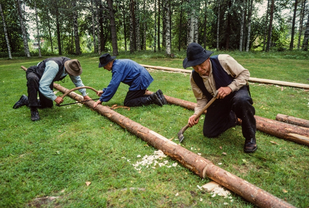 Ola Kolstad, Bjørn Haugen og Kjell Haugen fra Nord-Odal lager flisbane i Norsk Skogmuseums friluftsmuseum på Prestøya i Elverum sommeren 1998. De har lagt emneved – som tradisjonsbærerne kaller «flisrajer» – etter hverandre i linje på ei grasslette.  Karene boret hull i rajene og slo plugger av ospevirke gjennom disse hullene og ned i bakken, slik at rajene lå stabilt.  Deretter ble ujevnheter i skjøtene mellom flisrajene telgjet plane med øks, noe Kjell Haugen arbeidet med i forgrunnen (tl høyre) da dette fotografiet ble tatt.  Til venstre ser vi Ola Kolstad og Bjørn Haugen skjære hakk på tvers av rajene med cirka 50 centimeters mellomrom ved hjelp av ei bogesag.  Når dette var gjort kunne «kjøringa» starte.  Flisa ble produsert ved hjelp av en diger høvel – en såkalt «flisokse» – som ble trukket over rajene mens en mann kjørte hestene, en styrte flisoksen og en satt på den, slik at den lå «godt nedåt» og etterlot seg flis med jevn tjukkelse på cirka fem millimeter.  Når de første flisrajene var høvlet nesten ned til kjernen, ble de brukt som underlag for neste lag av flisrajer, som ble festet på de underliggende ved hjelp av ospeplugger.  Flisbanen besto av flisrajer i to parallelle linjer, slik at flisoksen kunne kjøres «fram» på den ene og «attende» på den andre.  Fotografiet er tatt i under opptakene til en instruksjonsfilm om produksjon av takflis og legging av takflis, og karene hadde kledd seg i antrekk som gav assosiasjoner til ei tid da bruken av et slikt taktekkingsmateriale var langt mer utbredt enn på opptakstidspunktet. 