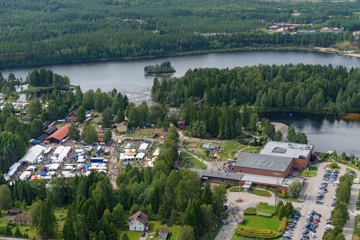 Norsk Skogmuseum i Elverum, sett fra lufta, 9. august 2014.  Fotografiet er tatt fra øst på lørdagen under De nordiske jakt- og fiskedager dette året, noe som preget aktiviteten på museet og i området omkring.  Museumsbygningene, to blokker på 40 X 40 meter, utført i betong med teglsteinsforblending, ligger til høyre i forgrunnen.  På parkeringsplassene øst og nord for bygningene var det parkert biler.  Sør for museumsbygningene (til venstre), på det som en gang var åkerarealer på klokkergarden Fossum (til venstre i forgrunnen), var det telt som var utsalgssteder for mange av arrangementets utstillere, omkranset av mange mennesker.  Også i friluftsmuseets på Prestøya i Glomma var det mange to- og firbeinte denne dagen, for jakthundeutstillingen hadde bortimot 700 påmeldte.  

Den dagen dette fotografiet ble tatt var det 13 148 gjester som løste billetter til De nordiske jakt- og fiskedager.  I løpet av de fire dagene arrangementet pågikk var det 31 919 mennesker som besøkte museet. 