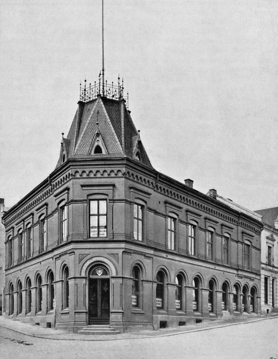 Forretningsgården til Skiensfjordens Kreditbank i Skien, fotografert i slutten av 1890-åra.  Dette er en hjørnegård, oppført i litt hellende terreng.  Bygningen har to etasjer og later til å være utført i pusset teglsten.  Fasadeuttrykket preges av historismen, som var en dominerende stilart for bygårder i murverk da denne bygningen ble reist, i 1888-1889.  I første etasje har den rundbuete, romansk inspirerte vinduer, og ved døråpningen på det «brukne» hjørnet mot foranliggende gatekryss.  I annen etasje er vindusåpningene rektangulære og har krysspostvinduer. Med fordakninger over.  Gesimsen er prydet med et framspringende, murt buemønster i tegl.  På taket er bygningens hjørneparti – og dermed også hovedinngangen i første etasje – markert med et teglsteinstekket tårnoppbygg med små, triangulære vinduskasser på sidene og en liten platting på toppen, omgitt av et profilert smijernsrekkverk og med ei flaggstang på midten.  Skiensfjordens Kreditbank ble etablert i 1881 etter innbydelse til aksjetegning fra sentrale aktører i forretningslivet i denne regionen (Nils Aall [trelasthandler, Porsgrunn], Anthon Bruun [kolonialkjøpmann og skipsreder, Skien], Erik J. Cappelen [proprietær, Gjerpen], Hans Cappelens Enke [trelasthandlerfirma, Solum/Skien], Gunnar Knudsen, Hans Møller [forsikringsagent og skipsreder], Thomas Offenberg [kjøpmann og skipsreder, Skien], Constantius Thrane Riis [kjøpmann og skipsreder, Skien], Johan Schaaning [skipsreder, Skien] og Mathias Vauvert [trelasthandler, Porsgrunn]).  Banken ble etablert med en aksjekapital på 2 millioner kroner, en kapitalbase som i 1890 ble økt til 3 millioner kroner.  I begynnelsen leide banken lokaler i trelasthandler og skipsreder Christopher H. Bloms gård i Prinsens gate i Skien.  I 1889 flyttet Skiensfjordens Kreditbank egen, nybygd gård (jfr. fotografiet) på hjørnet mellom Ligata og Skistredet i Skien.  I 1914 hadde banken også filialer i Porsgrunn og Kragerø, samt på Notodden og Såheim (Rjukan).  Fotografiet er lagt inn i Norsk Skogmuseums fotodatabase fordi Skiensfjordens Kreditbank tidlig på 1900-tallet var bankforbindelsen til Skiensvassdragets Fellesfløtningsforening. 