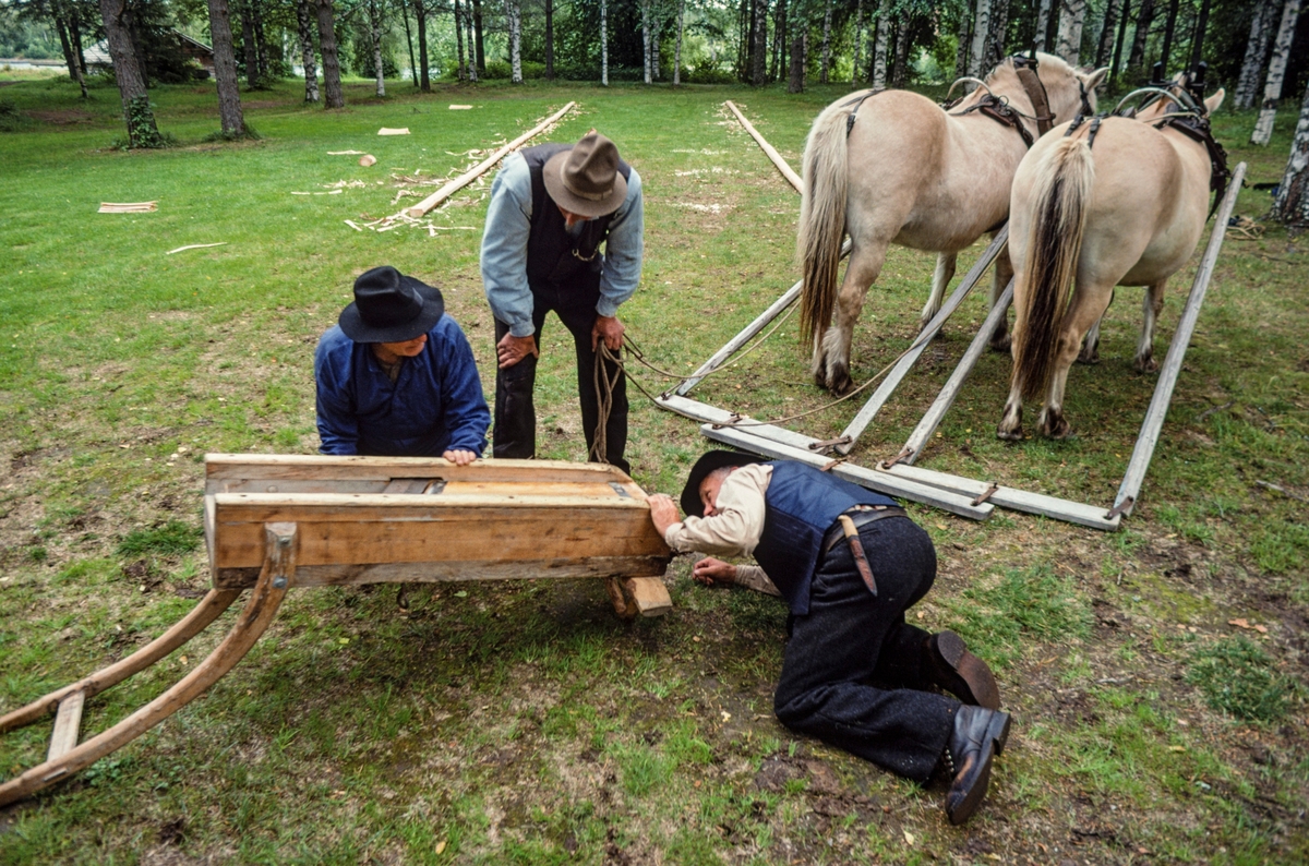 «Flisoksen» - en diger høvel – etterses og justeres for brukt på en flisbane som ble etablert i Norsk Skogmuseums friluftsavdeling på Prestøya i Elverum i forbindelse med opptakene til den kulturhistoriske dokumentasjonsfilmen «Flisbane og flistak – fra emne til ferdig tak» sommeren 1998.  På bildet ser vi Kjell Haugen fra Nord-Odal som ligger på knærne og sikter, antakelig for å forsikre seg om at høveltanna er stilt i en slik posisjon i forhold til sålen på høvelen at en kunne regne med å få flis av høvelig tjukkelse.  Sambygdingen Bjørn Haugen holdt flisoksen, som lå opp-ned, mens hestekaren Ola Kolstad sto ved siden av og fulgte prosessen med interesse.  Til høyre for ham ser vi de to fjordingene som ble brukt under arbeidet og dragene med hummul for tospann som ble brukt under arbeidet.  På sletta i bakgrunnen ser vi hvordan de lange, rette granstammene ("flisrajer") som skulle bli til takflis var montert, parallelt med noen meters mellomrom, slik at flisoksen kunne kjøres «fram» på den ene og «tilbake» på den andre.