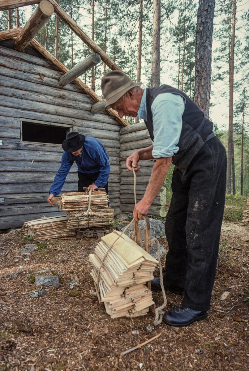 Bjørn Haugen (til venstre) og Ola Kolstad fra Nord-Odal, fotografert under løsning av takflis de nettopp hadde båret til på bæremeiser til ei kole som skulle få nytt flistak.  Den halvmeterlange takflisa, som var fordelt på to stabler på bæremeisene, var festet med tau som var spent mellom nedre og øvre rammetre på meisene.  Her knyttes tauene opp foran koia.  Karene var kledd i arbeidsklær som henspilte på mellomkrigstida, da de hadde opplevd legging av flistak som levende tradisjon.  Bjørn Haugen var iført mørke vadmelsbukser, blå busserull og en svart filthatt.    Også Ola Kolstad var kledd i mørke varmelsbukser, men han hadde lys skjorte og gråsvart vest på overkroppen og en grå filthatt på hodet.  På koia i bakgrunnen hadde karene tatt av det eldre flistaket og skiftet ut enkelte av sperrene på det kombinerte ås- og sperretaket før dette fotografiet ble tatt.  Før ny flis kunne legges måtte taket også lektes på nytt.  Fotografiet er tatt under opptakene til den kulturhistoriske dokumentasjonsfilmen «Flisbane og flistak – fra emne til ferdig tak» sommeren 1998.

Koia står nå ved Malungen i Romedal allmenning, men den skal være flyttet dit i nyere tid fra en annen lokalitet i allmenningen.