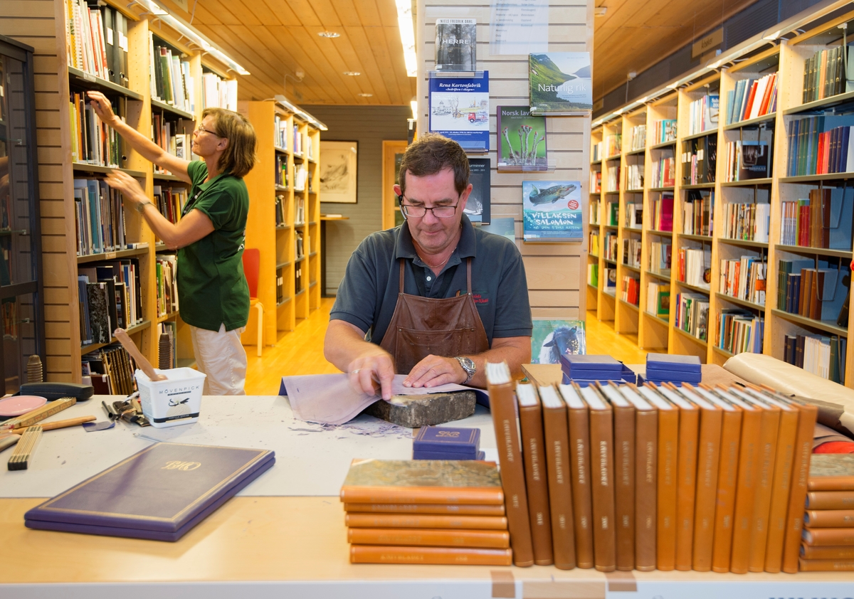 Bokbindermester Stein Julius Johansen fra Julius Ørenberg bokbinderi AS på Frysja i Oslo demonstrerer håndverket sitt i Norsk Skogmuseums bibliotek under De nordiske jakt- og fiskedager 2014.  Bokbinderen er medlem av Norsk knivforening, og foran seg på arbeidsbordet har han satt opp en del innbundne årganger av foreningens tidsskrift «Knivbladet».  Ved siden av seg har han fire etuier i blått lær, et produkt han leverer til Nobelkomitéen, som bruker dem som emballasje for Nobel-medaljene.  I hendene har han et lærstykke som han falser med ei flat steinplate som underlag.