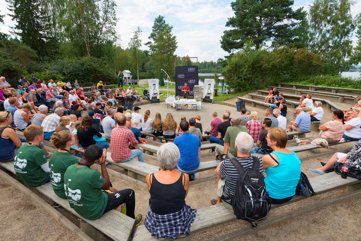 Kokken Daniél Rougé Madsen viser tilberedning av viltretter i friluftsamfiet på Norsk Skogmuseum i Elverum under De nordiske jakt- og fiskedager i 2014.  Fotografiet er tatt fra en posisjon bakerst i amfiet, mot amfigolvet, der Madsen hadde tatt oppstilling bak et bord og foran bannere som promoterte ham som kokk.  Madsen begynte som kokkelærling ved Hotel Residence i Sandnes.  Seinere har han arbeidet ved stjernekokken Michel Rouxs’ The Waterside Inn i Bray i England, og han har vært en sentral aktør i matprogrammer i tysk og fransk fjernsyn.  Da Daniél Rougé Madsen besøkte jakt- og fiskedagene hadde han også innledet et samarbeid med skuespilleren og jegeren Stig Henrik Hoff og fjernsynskanalen TV2 om programserien «Helt vilt», der Madsen skulle tilberede retter av råvarer fra norsk natur.