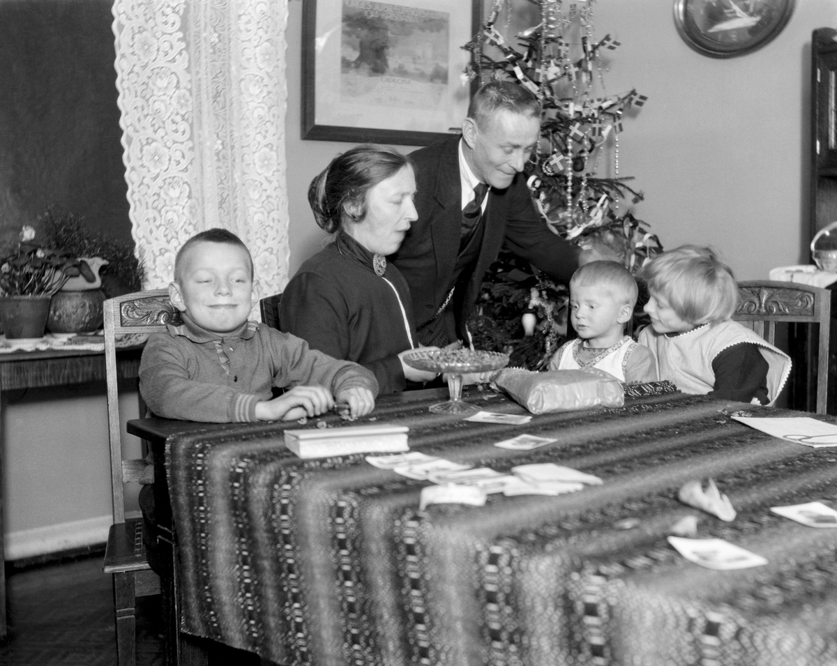 Julestemning hos familien Midttun i Telemark i 1925.  Fotografiet er tatt i spisestua, der barna Odd (til venstre), Magne og Bodil satt ved bordet sammen med mora Anne, mens fylkesskogmester Jørund Midttun sto ved bordenden, bøyd mot de to yngste barna.  På spisebordet lå det en vevd duk, og oppå den igjen lå ei bok og noen papirer.  På hjørnet der familien var samlet sto det dessuten et stettfat av pressglass med nøtter på.  I hjørnet bakenfor ser vi juletreet, ei gran som blant annet var pyntet med flagg og glitterbånd.