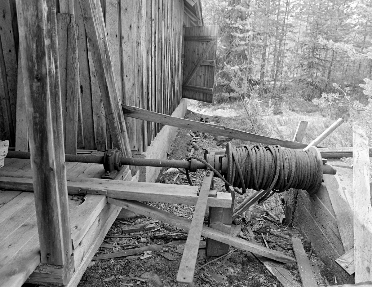 Fra Mastveltsaga i Åsnes.  Fotografiet er tatt ved den ene langveggen på saghuset, der det stikker ut en aksling med en støpejernvalse som er påviklet en del vaier.  Sentralt i forgrunnen ser vi også ei jernstang, som muligens ble brukt ved manøvrering av denne innretningen, som antakelig ble brukt til å trekke tømmer mot sagbenken (kjerrat).  Den nærmeste delen av saghuset var en åpen bindingsverkskonstruksjon, mens den delen der lokomobilen sto var kledd med vankantet over- og underliggerpanel og hadde inngang via ei labankdør. Trongaardsaga.

Mer informasjon om Mastveltsaga og om lokomobilsager generelt finnes under fanen «Opplysninger».