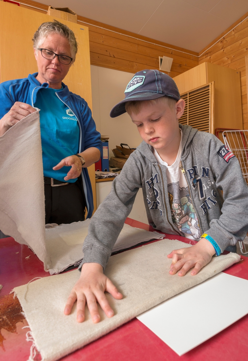 Fra det såkalte «papirkjøkkenet» ved Klevfos Industrimuseum på Ådalsbruk i Løten, Hedmark.  Fotografiet viser en gutt fra 2. trinn ved Stavsberg skole i Furnes (Ringsaker kommune), som bretter filt rundt et vått flak med papirmasse, som han nettopp hadde hentet opp fra et kar ved hjelp av ei finmasket nettingramme.  Papirarkene skal deretter settes i press.  Museumsformidler Trine Edvardsen (til venstre på dette bildet) hjalp elevene gjennom denne prosessen.  Ved Klevfos Industrimuseum håndlages papir på denne måten som en introduksjon til hvordan papir framstilles i treforedlingsindustriens maskiner.  Prosessen med filtomslagene presenteres som en parallell til den prosessen som foregår i papirmaskinens pressparti.