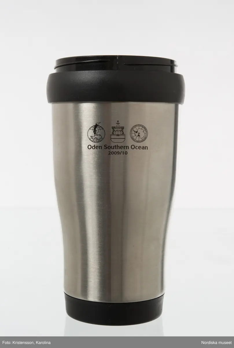 Termomugg av plast, med ytterhölje av aluminium. Används för varma drycker som kaffe och te. Locket saknas.