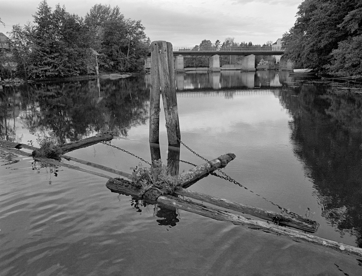 Ledelense og duc d’albe – pælebukk – i Strømselva i Aremark i Østfold, like ovenfor Strømsfoss lense.  Fotografiet er tatt høsten 1982, som var den siste sesongen det ble fløtet tømmer i Haldenvassdraget.  Tømmeret ligger inntil ei lense, der lensestokkene var lagt med endene om hverandre, som takstein.  Lensa hadde dessuten støttestokker som sto vinkelrett på lensestokken, på den sida det ikke skulle gå fløtingsvirke.  På andre steder lå endene av disse støttestokkene mot land, men her var det en duc d’albe (en pælebukk) med kjettingforbindelser til lensa som var støttepunkt.  Denne konstruksjonen skulle hindre at lensa og tømmeret ble presset i retning av elveløpet og Strømsfossen, til høyre i bildet, men i stedet ble ledet mot Strømsfoss lense til venstre.  På brua over elva (til høyre) går fylkesveg 124.  Bak det vestre bruhodet skimter vi litt av Strømsfoss mølle.Ledelense og duc d’albe – pælebukk – i Strømselva i Aremark i Østfold, like ovenfor Strømsfoss lense.  Fotografiet er tatt høsten 1982, som var den siste sesongen det ble fløtet tømmer i Haldenvassdraget.  Tømmeret ligger inntil ei lense, der lensestokkene var lagt med endene om hverandre, som takstein.  Lensa hadde dessuten støttestokker som sto vinkelrett på lensestokken, på den sida det ikke skulle gå fløtingsvirke.  På andre steder lå endene av disse støttestokkene mot land, men her var det en duc d’albe (en pælebukk) med kjettingforbindelser til lensa som var støttepunkt.  Denne konstruksjonen skulle hindre at lensa og tømmeret ble presset i retning av elveløpet og Strømsfossen, til høyre i bildet, men i stedet ble ledet mot Strømsfoss lense til venstre.  På brua over elva (til høyre) går fylkesveg 124.  Bak det vestre bruhodet skimter vi litt av Strømsfoss mølle.

En liten historikk om tømmerfløting og kanaliseringsarbeid i Haldenvassdraget finnes under fanen «Opplysninger».