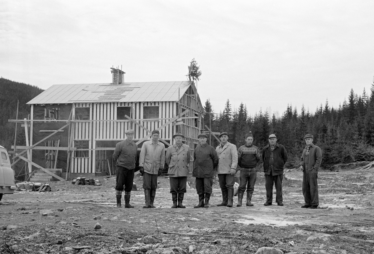 I 1959 inngikk den driftstekniske avdelingen i Der norske skogforsøksvesen avtale med Kirke- og undervisningsdepartementet om bruk av prestegardsskogene i Eidsvoll og Hurdal som driftstekniske forsøksskoger, i første omgang for en periode på 25 år.  Noe av det første Skogforsøksvesenet gjorde var å bygge driftsbygninger og boliger til personalet som skulle betjene forsøksskogene.  Dette fotografiet viser det kombinerte verksted- og garasjebygget ved det man kalte «Driftssentralen i Hurdal».  Fotografiet er tatt i forbindelse med kranselaget som ble avviklet da bygningen var under tak, 6. november 1960.  Karene som sto på rekke foran huset var antakelig lokale handverkere som hadde deltatt i byggeprosessen.