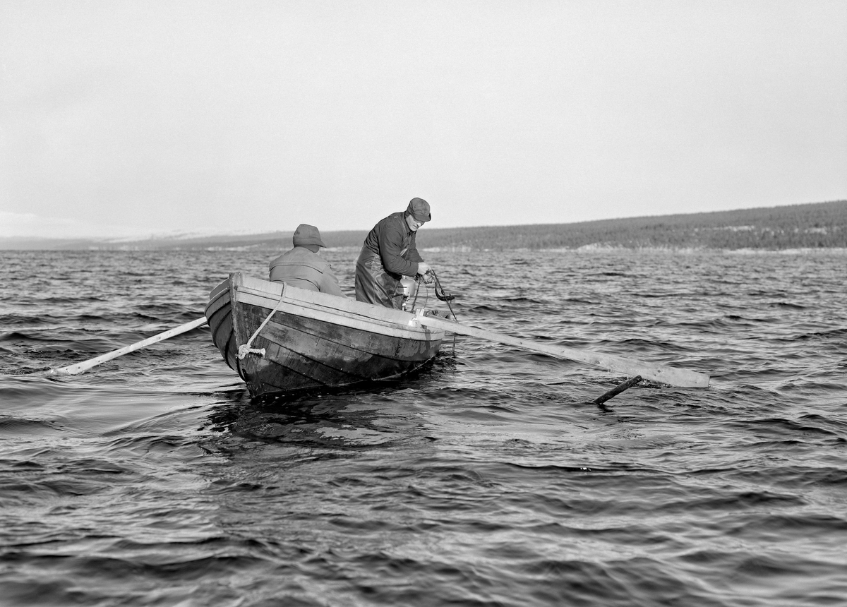 Røyefiskerne Oddmund (1913-1993) og Ottar (1921-2003) i båt på Femund i Engerdal høsten 1973.  Da dette fotografiet ble tatt satt Oddmund og rodde langsomt mens Ottar sto i akterenden og dro et garn med sprellende røye opp i båten.  Fiskerne var kledd i vindjakker og hadde luer med ørelapper.  Ottar hadde dessuten dratt på seg gummibukser for å skjerme seg mot vannspruten.  En slik påkledning kom vel med, for dette fisket foregikk i gytetida seinhøstes, fra midten av oktober til litt ut i november.  På denne årstida kunne det være temmelig kaldt og trekkfullt på den over 200 kvadratkilometer store innsjøen 662 meter over havet.  De snødekte høgdedraga i bakgrunnen bekrefter at dette fisket foregikk i kalde omgivelser.  «Femund-røya er feit og fin og rød i kjøttet som nyskåret oksefilet, og så ettertraktet at det aldri kan skaffes nok av den», sto det i en avisreportasje de fra den søndre delen av sjøen det året dette fotografiet ble tatt.  Mye av fangsten ble til rakfisk som ble solgt i hele Hedmark.  Fisket foregikk på grunner i sjøen, som gardene og familiene som bodde på dem hadde hevd på.  I begynnelsen av 1970-åra var det rettslig strid mellom brukerne på garder i Rendalen som hadde hatt sesongfiske i Femund før gardsbrukene ved innsjøen ble ryddet på 1700- og 1800-tallet og beboerne på disse eiendommene om fiskerettigheter.  Fisket foregikk tradisjonelt i samarbeid mellom flere aktører i robåter med to roere og en som handterte garna.  Etter påhengsmotorenes inntreden greidde man seg med to mann i hver båt.  Det året dette fotografiet ble tatt overtok Norsk Skogbruksmuseum ei «nettbu» eller «røykbu» der brødrene Riseth brukte å tørke nettene (fiskegarna) sine, mot å bekoste ei ny bu.  Dette fotografiet er sannsynligvis tatt da fagfolk fra museet besøkte brødrene for å besiktige så vel bua som fisket.