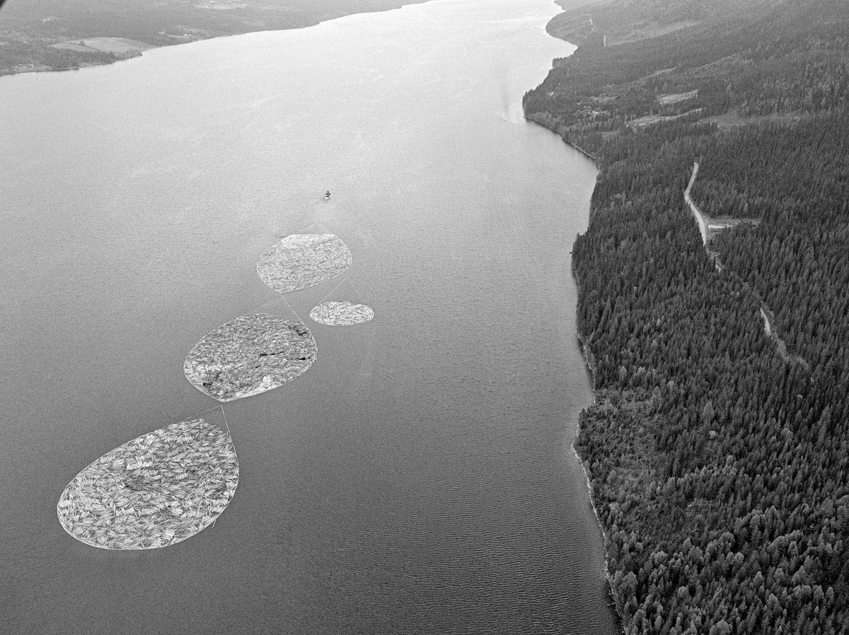 Flyfotografi av slepebåten «Storsjø» på innsjøen  i Rendalen som den hadde fått navn etter.  I ei trosse bak i god avstand bak «propellvannet» bak fartøyet hang slepet, som besto av tre mellomstore og en liten ringbom med fløtingstømmer.  Slepene var tunge.  I dampdriftsperioden, som for Storsjøs del varte fra 1912 til 1956, tok slepinga lang tid.  Dampmaskinen slukte nemlig 16 kubikkmeter ved i døgnet, og båten måtte gjerne ankres opp for bunkring av mer ved fra lagre langs strendene sørover.  I dieselepoken (fra 1957) brukte Storsjø brukte gjerne 30-40 timer på å buksere tømmer fra Åsheim i nordenden av sjøen til Åmot-grensa 36 kilometer lengre sør.  Gjennomsnittshastigheten var med andre ord cirka 1 kilometer i timen.  Tilbaketuren nordover sjøen, uten slep, var vanligvis unnagjort på to og en halv time. Slepetida var for øvrig avhengig av vær og vind, og av mannskepenes evne til å følge strømdraget i sjøen, den såkalte «råka».  I kraftig vind kunne bommene ryke, slik at løstømmeret ble spredt ut over sjøens vannspeil.  Under slike værforhold svarte det seg å legge båten og slepet mot land og vente på at vinden spaknet, eller rett og slett å la ringbommene flyte fritt.  Med den driftsaktiviteten som foregikk i rendalsskogene i 1950-åra kunne det går over tredve slike slep over Storsjøen i løpet av en sesong.  De siste åra, da det bare var massevirke til Borregaard som fortsatt ble fløtet, var antallet slep redusert til om lag en tredel av dette.  Fra gammelt av ble det sagt at det kunne gå 12-15 000 tylfter tømmer i hvert slep, men med stadig større massevirkeandel ble det mer småtømmer og dermed flere stokker i ringbommene.  Det siste fløtingsåret, da dette fotografiet ble tatt, var det cirka 17 000 kubikkmeter tømmer som skulle bukseres over Storsjøen.

Mer informasjon om slepebåten «Storsjø» finnes under fanen «Opplysninger».