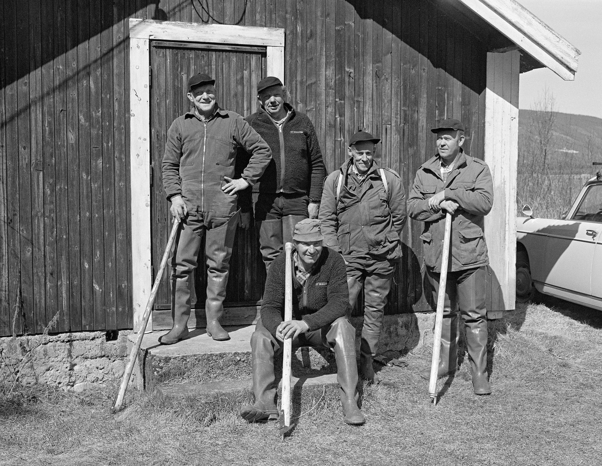 Fem tømmerfløtere fra Ytre Rendalen i Hedmark, samlet framfor Glomma fellesfløtingsforenings koie på Otnesøyen ved Lomnessjøen.  Stående fra venstre ser vi Kåre Hansen, Harald Hansen, Ola Stubsveen og Egil Berger.  På trappa foran dem satt Bjørn Brennodden.  Karene var arbeidskledde og tre av dem hadde kortskaftete fløterhaker i hendene.  Bildet ble tatt den siste sesongen det ble fløtet tømmer i denne delen av Glommavassdraget, nemlig i 1984.  Etter avviklinga av virksomheten kjøpte Rendalen kommune anlegget på Otnes med koie, smie, redskapsbu og en del utstyr med sikte på å bevare det som kulturminne.