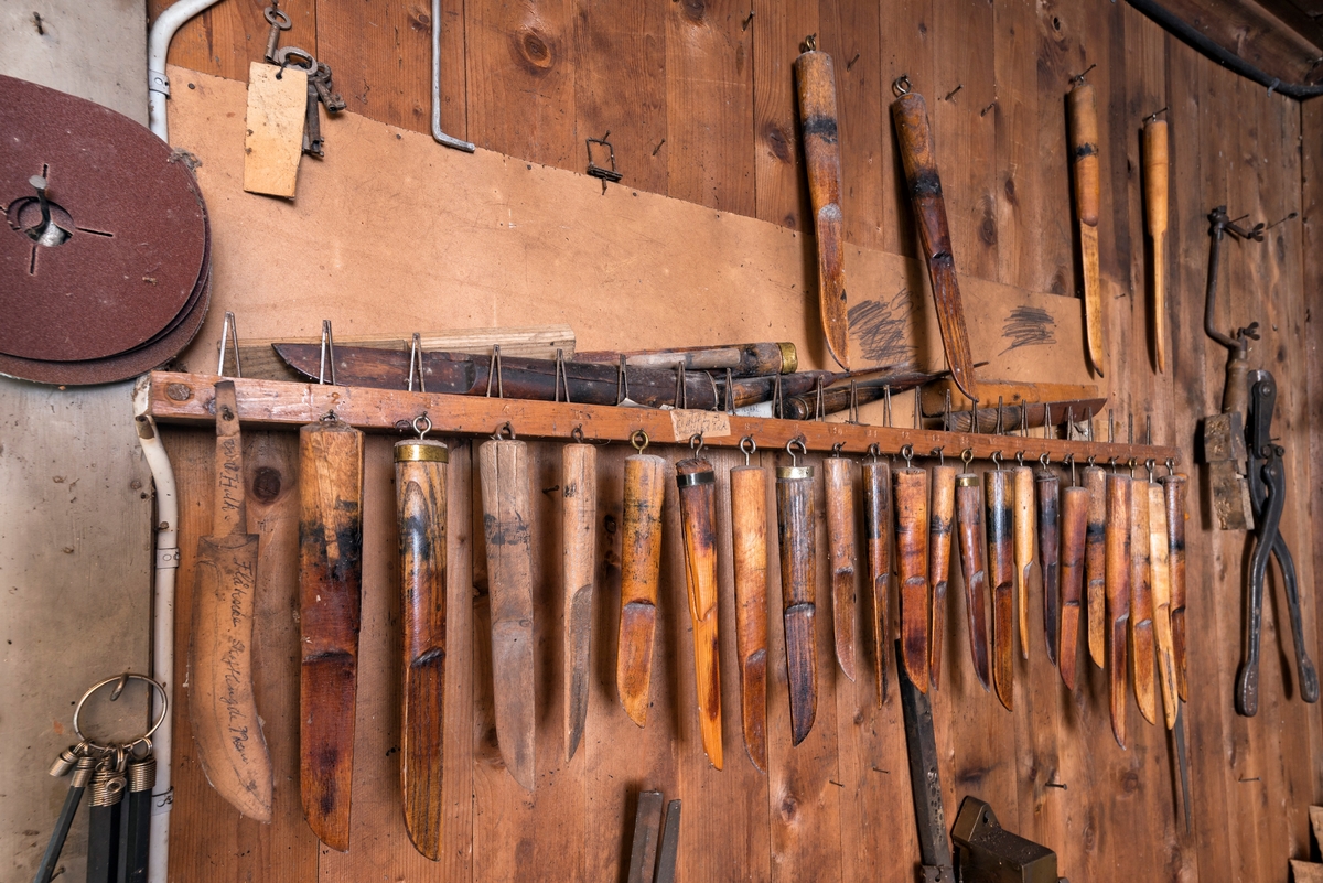 Detalj fra interiøret i verkstedet til knivmakeren Even Johannes Blindingsvolden (1908-1985) fra Ringsaker.  Bildet viser et utsnitt fra den nordvestre gavlveggen i verkstedrommet, der knivmakeren hadde lagd seg ei hylle hvor han hadde lagt og hengt opp cirka 30 ulike maler han brukte under slireproduksjon.  Malene er lagd av harde treslag, og de er tydelig preget av mangeårig bruk.  Blindingsvolden eide og bodde på småbruket Rudsland på Rudshøgda.  Her hadde han et et 43 kvadratmeter stort hus ved Prestvegen som inneholdt smie- og verkstedrom.  Dette bildet er tatt i det 24,5 kvadratmeter store verkstedrommet.

Mer informasjon om verksted- og smiebygningen, samt om knivmakeren Even J. Blindingsvolden finnes under fanen «Opplysninger».