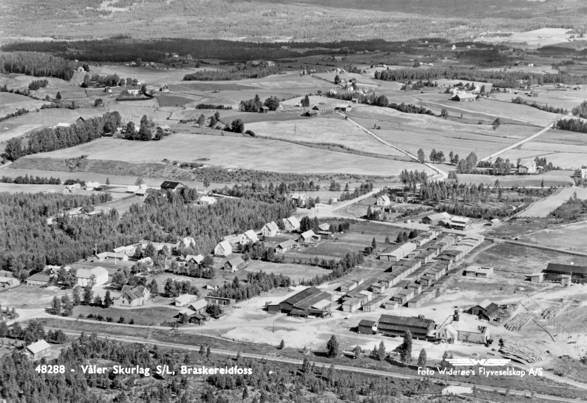 Flyfotografi tatt over produksjonsområdet til Våler Skurlag og den daværende på Braskereidfoss i Solør omkring 1950. Mot vest (ved nedre bildekant på dette fotografiet) avgrenses området av Solørbanen, som går parallelt med Glomma i retning nord-sør. Sentralt i forgrunnen, øst for jernbanelinja, ser vi et materiallager (bygd 1932) og ei rekke med digre materialstabler østover mot gjennomfartsvegen gjennom Solør (Riksvei 2, som seinere er flyttet litt lengre mot øst for å gi mer areal til sagbruket og sponplatefabrikken som ble etablert her i slutten av 1960-åra). Til høyre i forgrunnen, lå en sag- og høvleribygning, som antakelig ble oppført i 1932, og i forlengelsen av dette ser vi fyr- og maskinhuset, som var oppført i teglmur ti år seinere.  Lengst sør på sagtomta, ved høyre bildekant, lå det nyeste av Våler skurlags daværende saghus (bygd 1942 for elektrisk drift, brannherjet vinteren 1964). Bygningen som mellom fyr- og maskinhuset og «nysaga» skal ha vært et mindre materialhus, som også fungerte som ekspedisjonslokale for lokale trelastkunder. Kornsiloen like sør for fyr- og maskinhuset, som seinere har vært et landemerke på området, ble først påbegynt i 1953. Til venstre i forgrunnen ser vi villabebyggelsen langs Braskereidvegen, som på østsida av Solørvegen går over i Gravbergsvegen (mot høyre bildekant), med Lundvegen som avstikker mot den mer sentrale den av bildet. I åkerlandskapet til venstre ser vi gardene Lundeby og Elset.