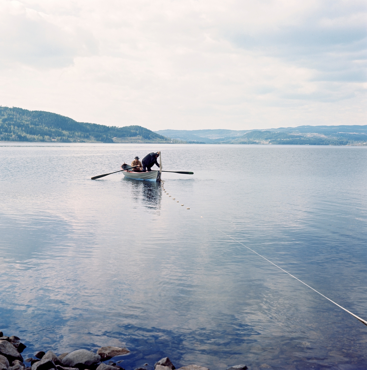 Notkast etter krøkle ved Langodden i Furnesfjorden i Mjøsa.  Fotografiet er tatt fra strandlinja.  I en robåt 10-15 meter utenfor ser vi to menn, en som ror og en annen som står og kaster nota overbord.  I forgrunnen til høyre ser vi det ene nottauet, som det antakelig var en fisker der som holdt.  Det andre nottauet ble seinere rodd i land etter at nota var kastet.  Ved inndraing ble den til en U-formet nettpose som fanget opp fisk i den innenforliggende strandsonen. 

Dette notkastet var nok et rekonstruksjonsforsøk knyttet til noe som hadde vært et tradisjonelt vårfiske i Furnesfjorden, antakelig fram til disse karenes barndom.  En del større garder hadde hevd på å drive såkalt «langrevfiske», en ferskvannsvariant av linefiske, utenfor sine strandlinjer.  I dette fisket brukte man levende krøkle som agn på langrevens kroker.  Krøkla ble fanget i nøter, som den vi ser på dette fotografiet, når den kom inn mot strendene for å gyte om våren. Denne formen for fiske opphørte etter at det ble forbudt å bruke levende agnfisk.  Karene på fotografiet hadde følgelig neppe vært med på notdraing etter krøkle.  De hadde imidlertid med seg en 90-årig veteran, som nok kunne fortelle hvordan det ble gjort (jfr. SJF-F. 007189).  Dette stedet ved Langodden skal ha vært et av Mjøsas beste krøklevarp.  Fiskeredskapen var antakelig utlånt fra boet etter brødrene Hans (1900-1966) og Martin (1904-1960) Storihle på garden Stor-Ile i Furnes.  Fra denne garden ble det drevet et omfattende fiske i Mjøsa, til dels med sikte på videresalg av fisk til kjøpmenn på Hamar og i Oslo.  Garden har fortsatt fiskerhytte på Langodden. 