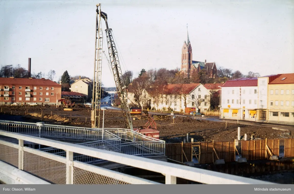 Vy mot nordväst, okänt årtal. Mark schaktas för nybygget av Mölndals Centrum, utefter bostadshusen på Bergmansgatan. Vägen fortsätter över Storgatan, förbi Sahlins terrass (låg byggnad mittemot rött tegelhus till vänster), och upp mot Frölundagatan. Fässbergs kyrka ses i bakgrunden.