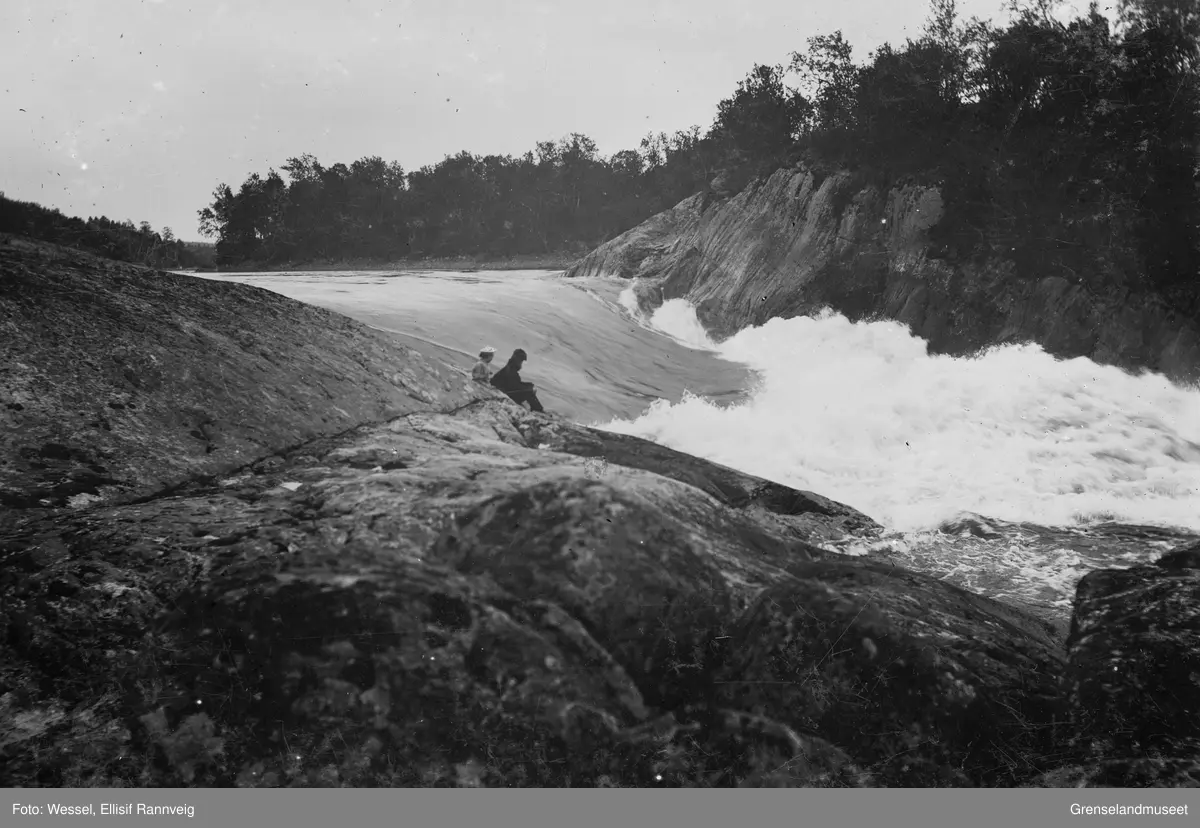 Harefoss i Pasvik. Et par sitter ved elvekanten og ser utover fossen.