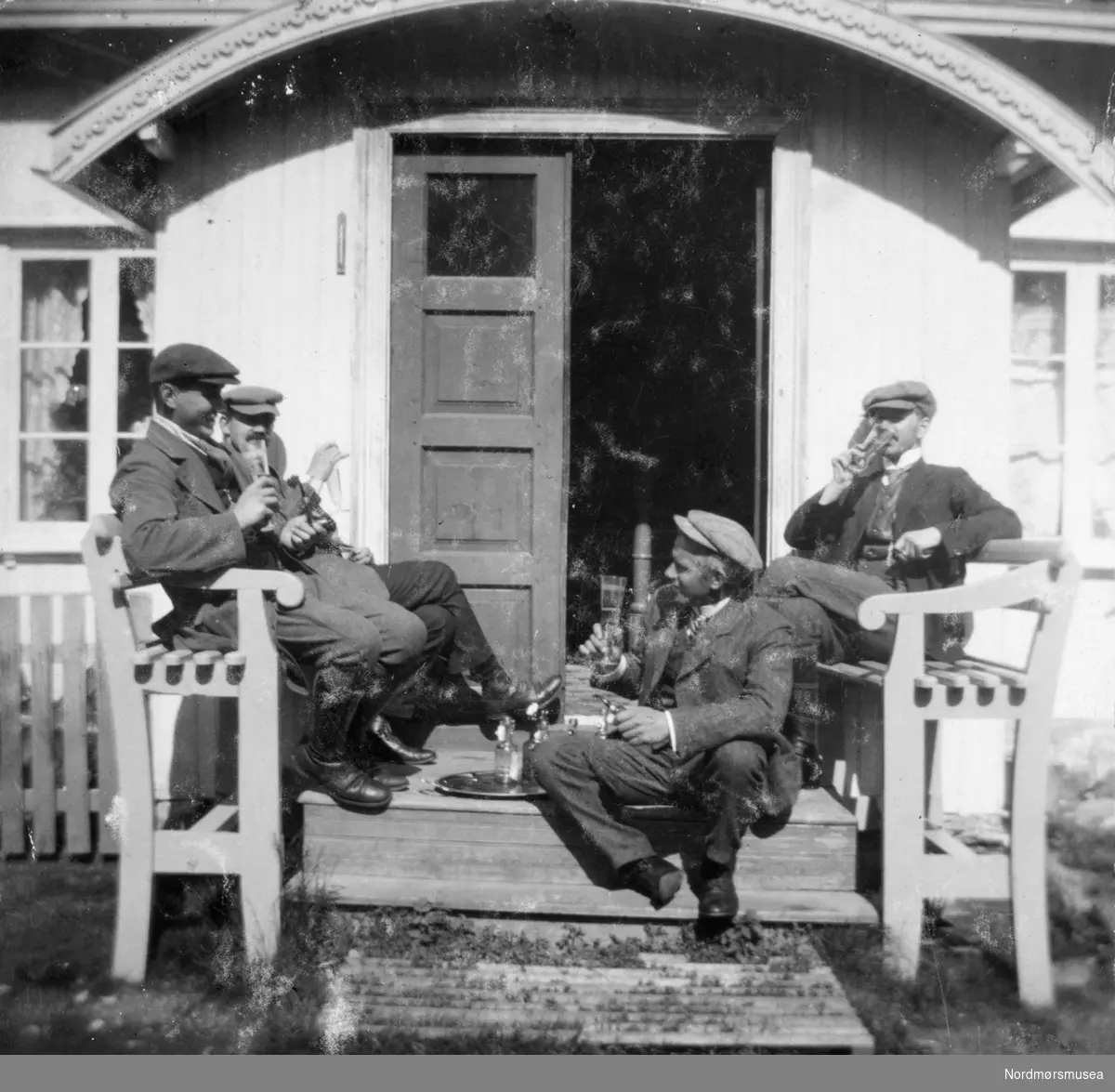 Foto av en gruppe menn på trappa til Randistua ved Enge Bruk i Valsøyfjord i Halsa kommune. Samling fotografier fra Enge Bruk i Valsøyfjord i Halsa kommune. Eier av originalmaterialet er Kolbjørn Botten. Fra Nordmøre museums fotosamlinger.