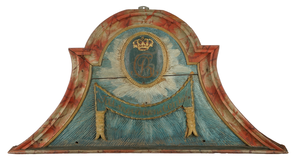 Døroverstykke bestående av 3 sammensatte trebord med not og fjær (bunnplaten). Det har en trekantet hovedform med rett underkant, innadbuede sider og utadbuet overkant. Bunnplaten er utskåret og i flere nyanser av blått, påsatt 2 forhøyninger. Den øverste er oval, blåmalt med krone i gull og rødt over "CR" påmalt i brunt, og langs kanten en lysutskåret bord. Den nederste er formet som en girlander og er avlang, buet og blåmalt med "Told-inspekteurens  Contoir" påmalt med brunfarge. Langs kanten er det en lysutskåret bord og på hver side en lys, utskåret dusk. Skiltet omgitt av en rett list i underkant samt en rød og grå buet, profilert list på sidene og i overkant. Disse er malt i noe som minner om en marmoreringsteknikk (bemalt imitasjon av marmor).Tilhører et sett med tre døroverstykker .Jfr. B-bok nr. 518,519,520. Nr. 518 er borte (ToldCassererens Contoir") Antatt fra Christiania iht. B-bok