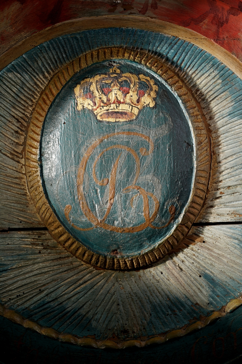 Døroverstykke bestående av 3 sammensatte trebord med not og fjær (bunnplaten). Det har en trekantet hovedform med rett underkant, innadbuede sider og utadbuet overkant. Bunnplaten er utskåret og i flere nyanser av blått, påsatt 2 forhøyninger. Den øverste er oval, blåmalt med krone i gull og rødt over "CR" påmalt i brunt, og langs kanten en lysutskåret bord. Den nederste er formet som en girlander og er avlang, buet og blåmalt med "Told-inspekteurens  Contoir" påmalt med brunfarge. Langs kanten er det en lysutskåret bord og på hver side en lys, utskåret dusk. Skiltet omgitt av en rett list i underkant samt en rød og grå buet, profilert list på sidene og i overkant. Disse er malt i noe som minner om en marmoreringsteknikk (bemalt imitasjon av marmor).Tilhører et sett med tre døroverstykker .Jfr. B-bok nr. 518,519,520. Nr. 518 er borte (ToldCassererens Contoir") Antatt fra Christiania iht. B-bok