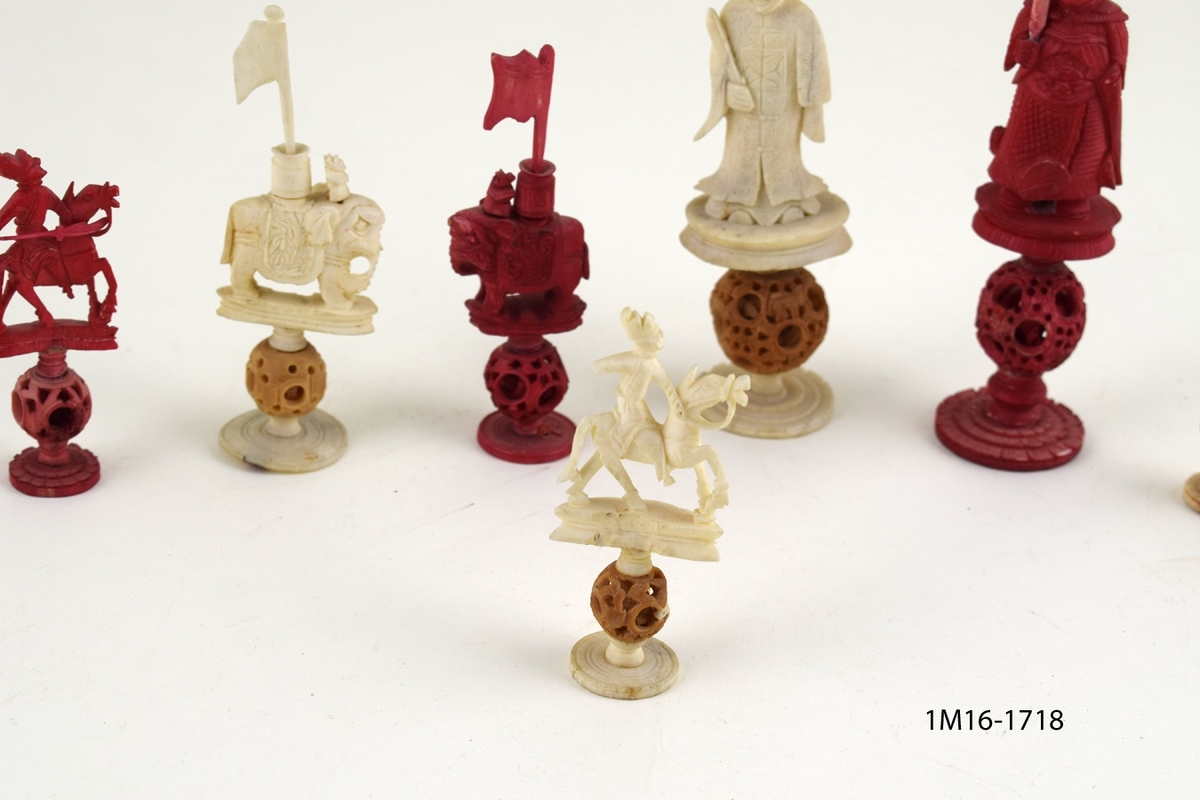 Röda och vita shackpjäser. Totalt 32 figurer. Figurerna i form av människor och elefanter. Minsta figuren 6cm. Största figuren 13 cm.