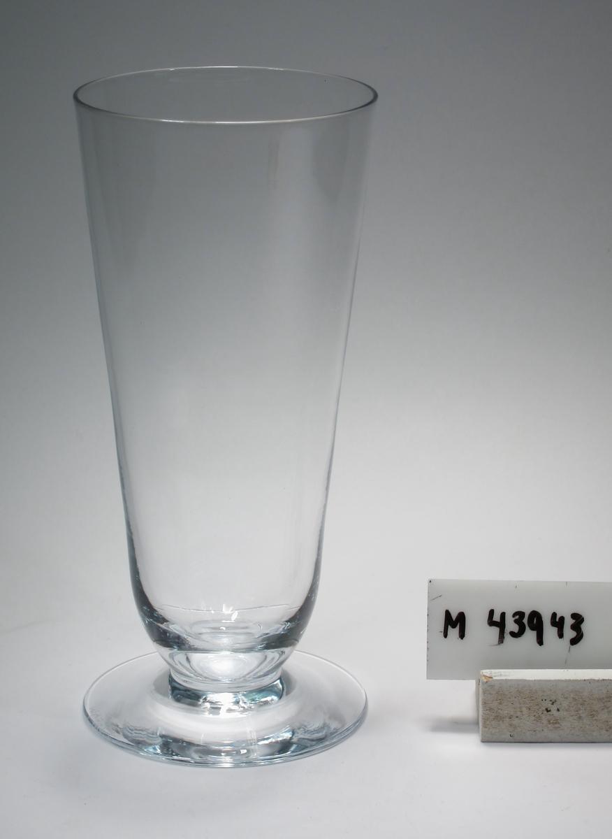 Ölglas.
Beskrivning: Konad kupa, trattformad fot, fotens kant ojämn.
Färg: Ofärgat klarglas.
Mått: Ovan anges mått för höjd och övre diameter. Bottendiameter: 68 mm.
Inskrivet i huvudkatalogen tidigast 1988.
SAKNAS VID INV. 2013-07-15
Funktion: Ölglas