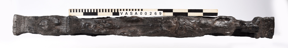 Skulpterad pilaster föreställande en herm eller möjligtvis en karyatid, under jonisk kapitäl.
Huvudet är vridet åt vänster samt prytt med en krona. Armarna hålls sträckta utefter sidorna.
Kroppen övergår i det med blad- och blomornamentik rikt sirade pilasterskaftet som smalnar av nedåt. Skaftet avgränsas genom en enkel vulst eller list från den rikt sirade och mjukt utbuktande piedestalen. Nedtill är piedestalen försedd med en bred bas. Skulpturens baksidan är slät.
Skulpturen är sliten.

Text in English: Sculptered pilaster with a Herm, or possibly a Caryatid, beneath an Ionic capital.
The head, with a crown, is turned to the left. The arms are streched out along the sides.
The body extends into the shaft of the pilaster, which tapers downwards and is richly decorated with leaf and flower ornamentation. A simple torus or batten separates the shaft from the richly decorated, softly bulging pedestal that has a broad base. The back of the sculpture is smooth.
The sculpture is worn.