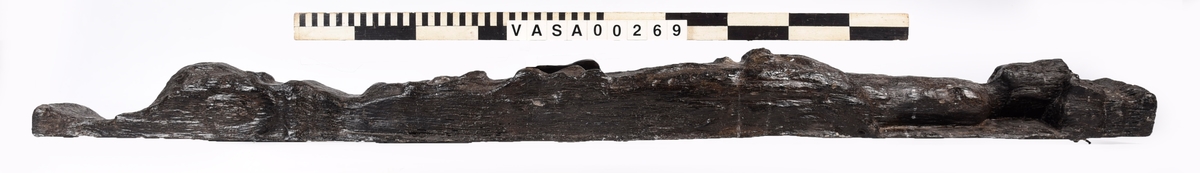 Skulpterad pilaster föreställande en herm eller möjligtvis en karyatid, under jonisk kapitäl.
Huvudet är vridet åt vänster samt prytt med en krona. Armarna hålls sträckta utefter sidorna.
Kroppen övergår i det med blad- och blomornamentik rikt sirade pilasterskaftet som smalnar av nedåt. Skaftet avgränsas genom en enkel vulst eller list från den rikt sirade och mjukt utbuktande piedestalen. Nedtill är piedestalen försedd med en bred bas. Skulpturens baksidan är slät.
Skulpturen är sliten.

Text in English: Sculptered pilaster with a Herm, or possibly a Caryatid, beneath an Ionic capital.
The head, with a crown, is turned to the left. The arms are streched out along the sides.
The body extends into the shaft of the pilaster, which tapers downwards and is richly decorated with leaf and flower ornamentation. A simple torus or batten separates the shaft from the richly decorated, softly bulging pedestal that has a broad base. The back of the sculpture is smooth.
The sculpture is worn.