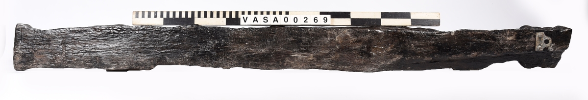 Skulpterad pilaster föreställande en herm eller möjligtvis en karyatid, under jonisk kapitäl.
Huvudet är vridet åt vänster samt prytt med en krona. Armarna hålls sträckta utefter sidorna.
Kroppen övergår i det med blad- och blomornamentik rikt sirade pilasterskaftet som smalnar av nedåt. Skaftet avgränsas genom en enkel vulst eller list från den rikt sirade och mjukt utbuktande piedestalen. Nedtill är piedestalen försedd med en bred bas. Skulpturens baksidan är slät.
Skulpturen är sliten.

Text in English: Sculptered pilaster with a Herm, or possibly a Caryatid, beneath an Ionic capital.
The head, with a crown, is turned to the left. The arms are streched out along the sides.
The body extends into the shaft of the pilaster, which tapers downwards and is richly decorated with leaf and flower ornamentation. A simple torus or batten separates the shaft from the richly decorated, softly bulging pedestal that has a broad base. The back of the sculpture is smooth.
The sculpture is worn.