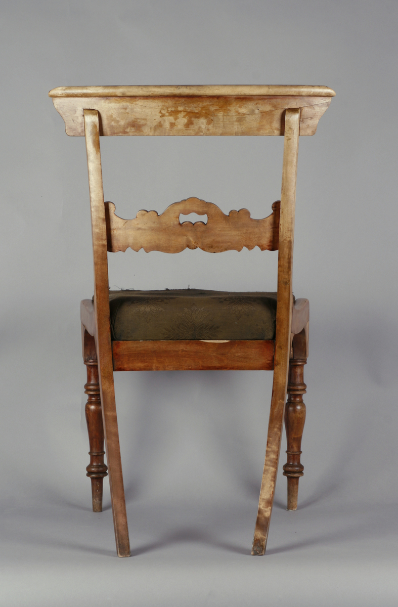 Biedermeier. Antatt bjørk med mahognybeis. Rett, noe tilbakeoverlenet, åpen rygg med utskåret midtsprosse. Det øvre tverrbrettet er glatt, noe svunget, og avrundet i hjørnene. Ingen armlener. Dreide, rette forben, lett bakoversvungne firkantede bakben. Stoppede seter, trukket med bomullsdamask. To av stolene trukket med sort trekk, to med mørkegrønt trekk.