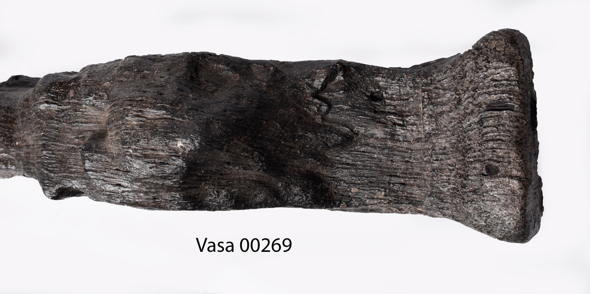 Skulpterad pilaster föreställande en herm eller möjligtvis en karyatid, under jonisk kapitäl.
Huvudet är vridet åt vänster samt prytt med en krona. Armarna hålls sträckta utefter sidorna.
Kroppen övergår i det med blad- och blomornamentik rikt sirade pilasterskaftet som smalnar av nedåt. Skaftet avgränsas genom en enkel vulst eller list från den rikt sirade och mjukt utbuktande piedestalen. Nedtill är piedestalen försedd med en bred bas. Skulpturens baksidan är slät.
Skulpturen är sliten.

Text in English: Sculptered pilaster with a Herm, or possibly a Caryatid, beneath an Ionic capital.
The head, with a crown, is turned to the left. The arms are streched out along the sides.
The body extends into the shaft of the pilaster, which tapers downwards and is richly decorated with leaf and flower ornamentation. A simple torus or batten separates the shaft from the richly decorated, softly bulging pedestal that has a broad base. The back of the sculpture is smooth.
The sculpture is worn.