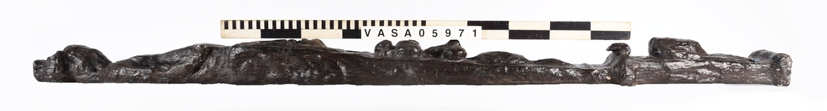 Skulpterad pilaster utformad som en karyatid med långt hår, troligen placerad under ett joniskt kapitäl.
Huvudet är vridet åt vänster. Höger arm är sträckt utefter sidan. Vänster arm är böjd och i handen håller figuren ett okänt föremål.
Pilasterskaftet är upptill prytt med en maskaron med bred, öppen mun och nedtill med en tung fruktfeston. Det nedåt avsmalnande pilasterskaftet avgränsas från piedestalen av en enkel vulst eller list med uppdragna kanter. Piedestalen är hög och jämnbred samt prydd med ett litet huvud och avslutas nedtill med en förtjockad bas. Skulpturens baksida är slät.
Skulpturen är kraftigt sliten och nött med finare detaljer utplånade.

Text in English: Sculpted pilaster with Caryatid with long hair under what is possibly an Ionic capital.
The head is turned to the left, the right arm is streched along the side, the left arm is bent and the hand holds an unknown object.
The shaft of the pilaster is decorated above with a mask with a broad, open mouth, below is a heavy festoon of fruit. The shaft tapers downwards and is divided from its pedestal by a simple torus or batten with drawn-up edges. The pedestal is high and even in width and decorated with a small head. It terminates at the bottom in a thickened base. Its back is smooth.
The sculpture is much worn, with finer details obliterated.