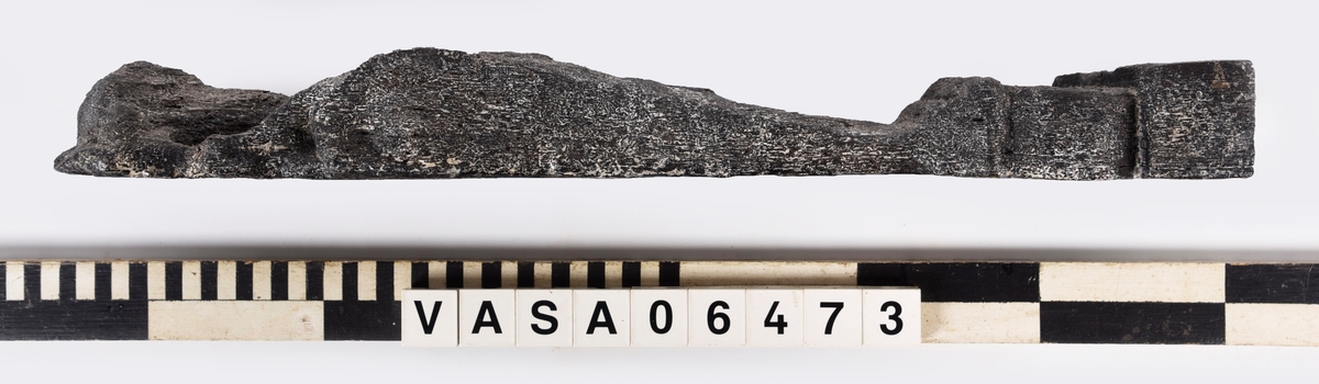 Liten skulpterad pilaster, utformad som en karyatid eller möjligen en putto. Figuren har långt hår och ett knubbigt ansikte, omgivet av en bred krage. Pilasterskaftet är dekorerat med akantusblad. Nedtill avslutas pilastern av en rikt profilerad och dekorerad sockel. Skulpturens baksida är slät.
Skulpturen är mycket sliten.

Text in English: A small carved pilaster, with a caryatid or probably a putto. The figure has a chubby face, long hair and a broad collar. The lower part of the pilaster is decorated with acanthus leaves. The figure stands on a richly profiled and decorated socle. The back of the sculpture is smooth.
The sculpture is very worn.