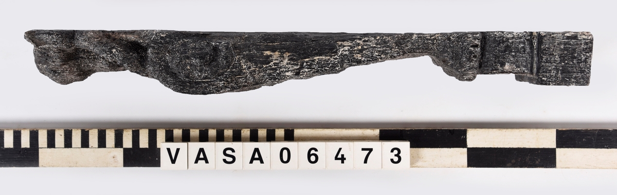 Liten skulpterad pilaster, utformad som en karyatid eller möjligen en putto. Figuren har långt hår och ett knubbigt ansikte, omgivet av en bred krage. Pilasterskaftet är dekorerat med akantusblad. Nedtill avslutas pilastern av en rikt profilerad och dekorerad sockel. Skulpturens baksida är slät.
Skulpturen är mycket sliten.

Text in English: A small carved pilaster, with a caryatid or probably a putto. The figure has a chubby face, long hair and a broad collar. The lower part of the pilaster is decorated with acanthus leaves. The figure stands on a richly profiled and decorated socle. The back of the sculpture is smooth.
The sculpture is very worn.