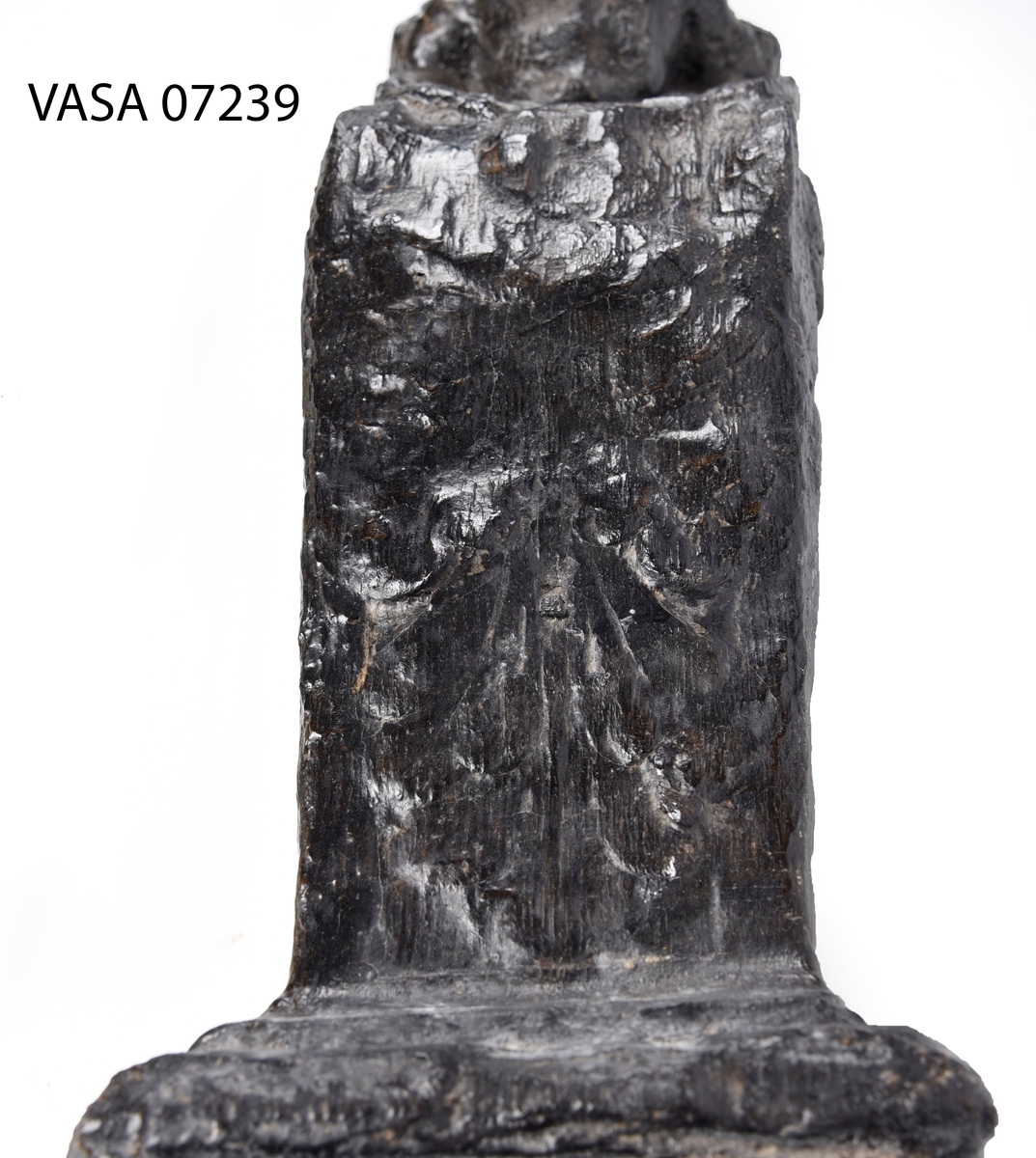 Liten skulpterad pilaster, utformad som en karyatid eller möjligen en putto. Figuren har långt hår och ett knubbigt ansikte, omgivet av en bred krage. Det nedåt avsmalnande pilasterskaftet är dekorerat med akantusblad. Nedtill avslutas pilastern av en rikt profilerad och dekorerad sockel. Skulpturens baksida är slät.
Skulpturen är sliten, främst den övre delen.

Text in English: A small carved pilaster, with a caryatid or probably a putto. The figure has a chubby face, long hair and a broad collar. The lower part of the pilaster is decorated with acanthus leaves. The caryatid stands on a richly profiled and decorated socle. The back of the sculpture is smooth.
The sculpture is worn.