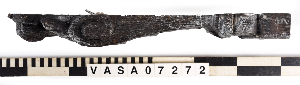Liten skulpterad pilaster, utformad som en karyatid eller möjligen en putto. Figuren har långt hår och ett knubbigt ansikte, omgivet av en bred krage. Det nedåt avsmalnande pilasterskaftet är dekorerat med akantusblad. Nedtill avslutas pilastern av en rikt profilerad och dekorerad sockel. På skulpturens släta baksida sitter en nygjord upphängningsanordning, fästad med två skruvar.
Skulpturen är sliten.

Text in English: A small carved pilaster, with a caryatid or probably a putto. The figure has a chubby face, long hair and a broad collar. The lower part of the pilaster is decorated with acanthus leaves. The caryatid stands on a richly profiled and decorated socle. On the smooth back of the sculpture is a new hanging device attached with two screws.
The sculpture is worn.